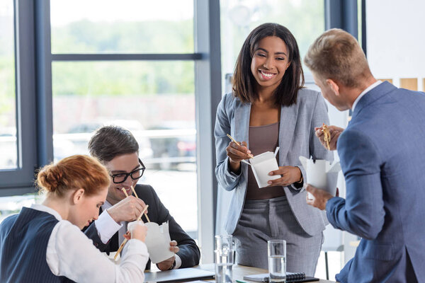 Бизнес-команда ест китайскую кухню во время перерыва на встречу в современном офисе
  