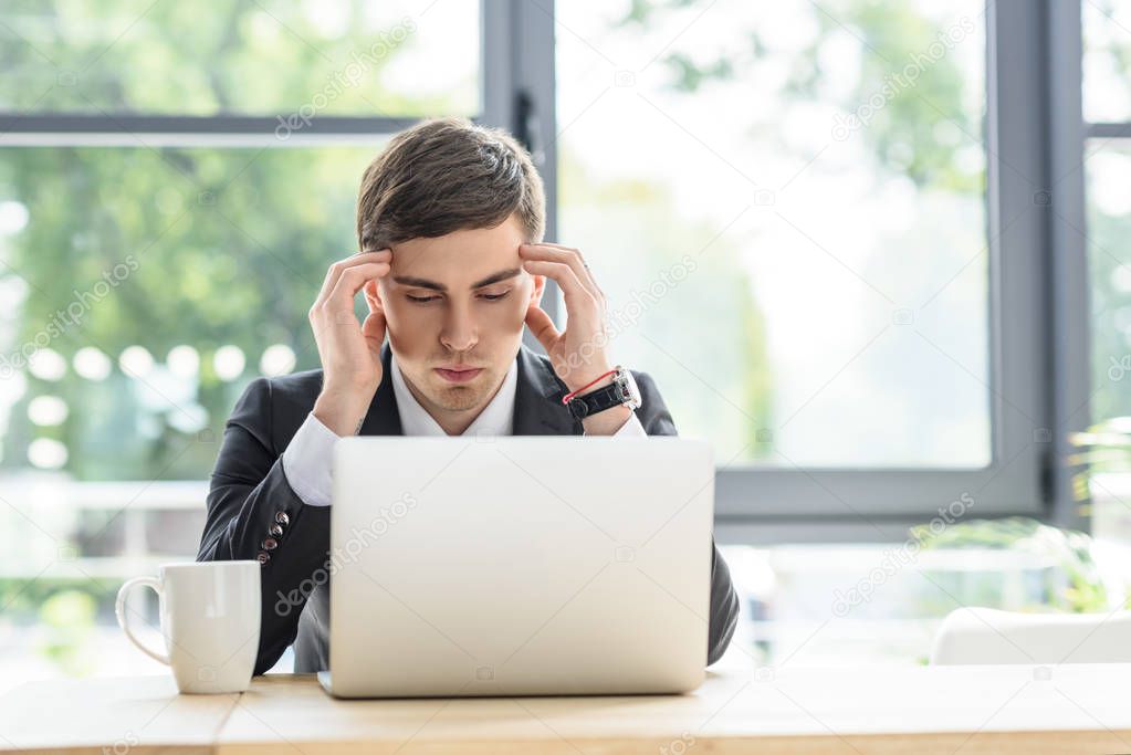 Businessman suffers from headache while working on laptop