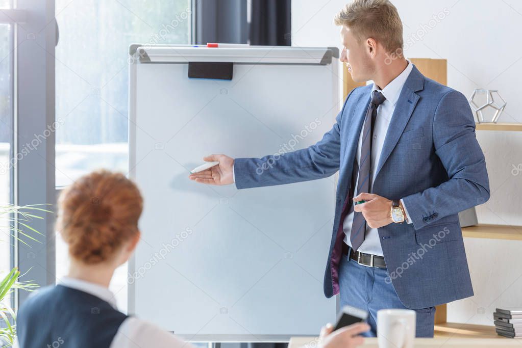 Young businessman presenting his idea by flip chart to colleagues in modern office