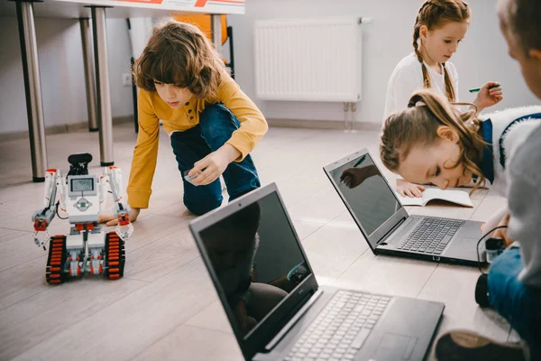 focused kids programming robots with computers while sitting on floor