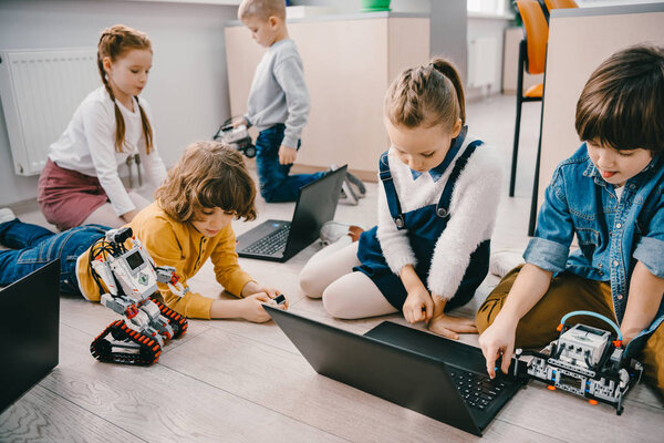 kids programming diy robots with laptops while sitting on floor, stem education concept