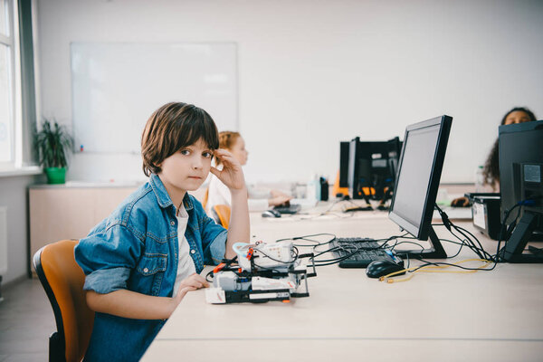 teen kid looking at camera while programming diy robot at machinery class