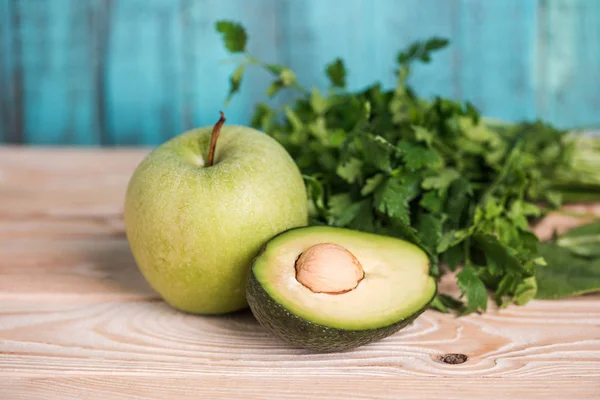 Aguacate maduro con perejil y manzana sobre mesa de madera - foto de stock