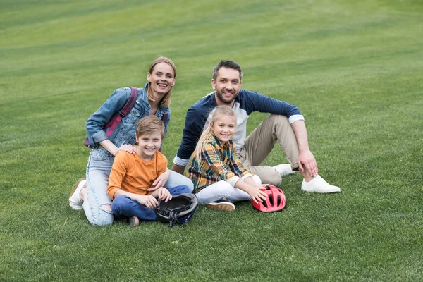 Famiglia sorridente seduta sull'erba al parco — Foto stock