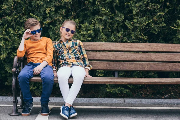 Niños adorables sentados en el banco en el parque - foto de stock