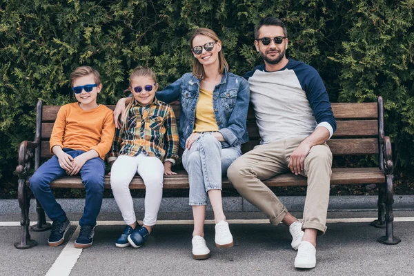 Famiglia sorridente in occhiali da sole seduto sulla panchina — Foto stock