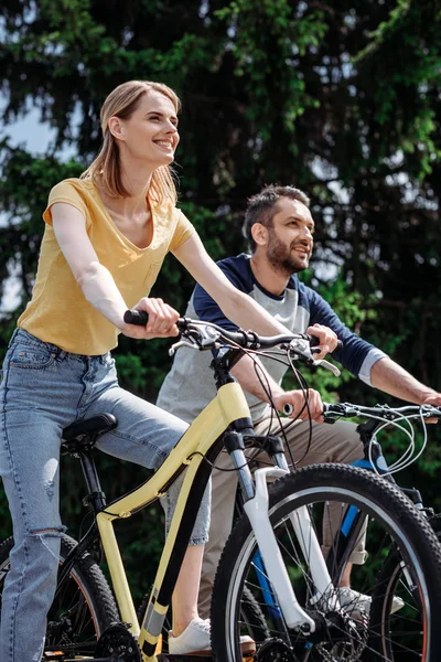 Улыбающаяся пара катается на велосипедах в парке — стоковое фото