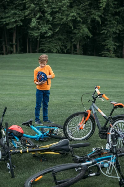 Niño niño de pie cerca de bicicletas en el parque - foto de stock