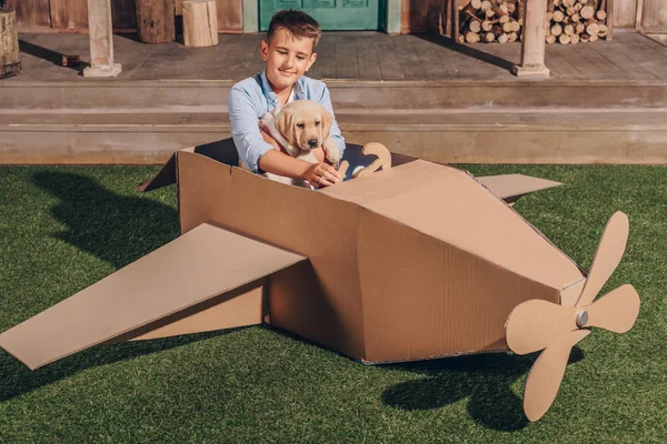 Хлопчик з цуценям у картонному літаку — стокове фото