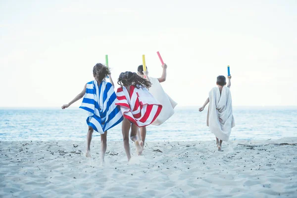 Niños con toallas corriendo en la playa - foto de stock