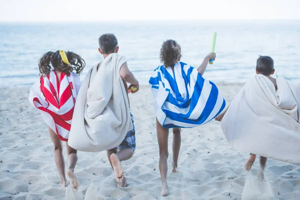 Children with towels running on beach — Stock Photo