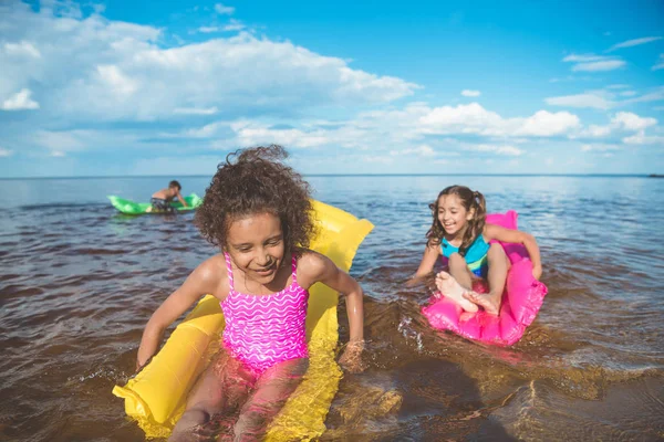 Niñas multiculturales nadando en colchones inflables - foto de stock