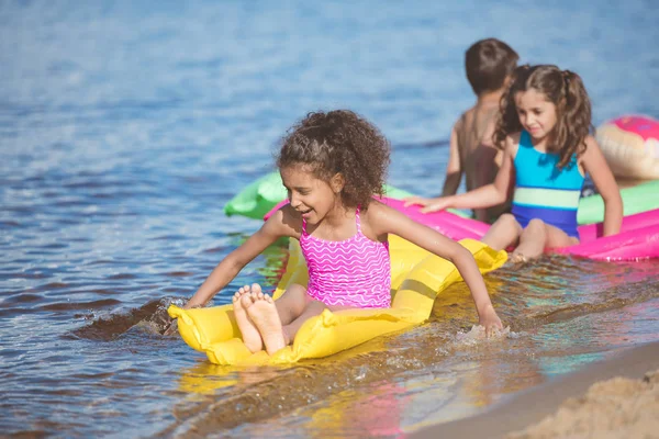 Niñas multiculturales nadando en colchones inflables - foto de stock