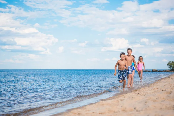 Niños multiétnicos corriendo en la playa - foto de stock