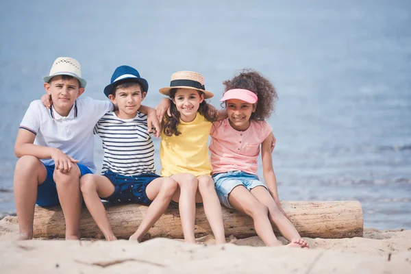 Enfants multiethniques assis au bord de la mer — Photo de stock