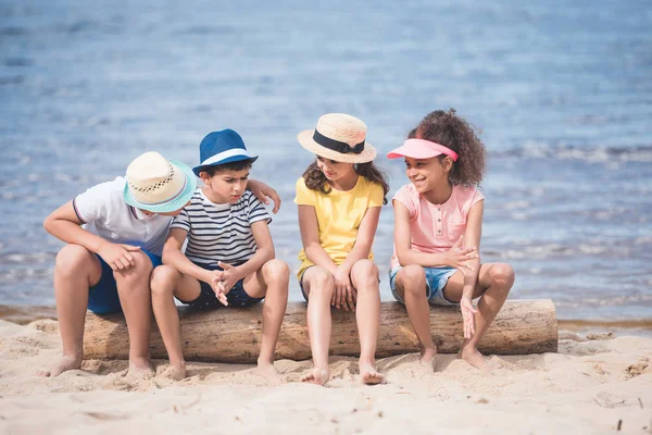 Niños multiétnicos sentados a la orilla del mar - foto de stock