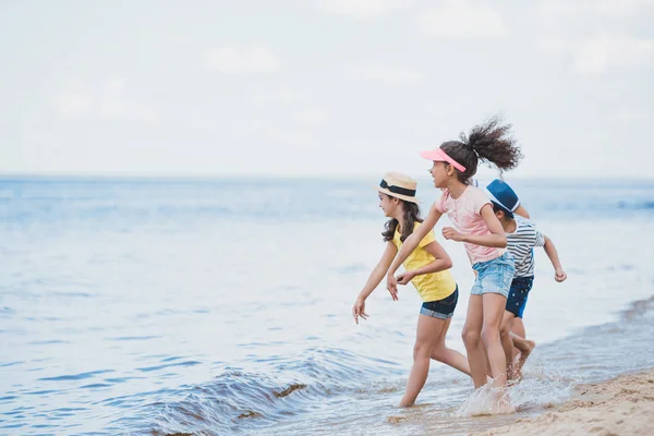 Crianças multiculturais jogando pedras à beira-mar — Fotografia de Stock
