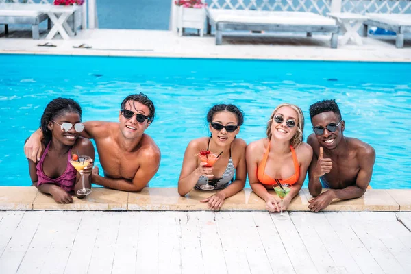 Multiethnic people with cocktails in swimming pool — Stock Photo