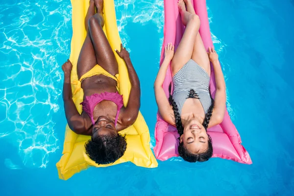 Multiethnic women on inflatable mattresses in pool — Stock Photo