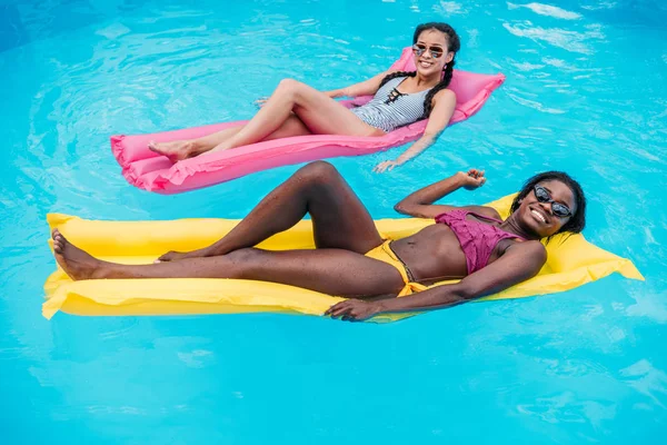 Multiethnic women on inflatable mattresses in pool — Stock Photo