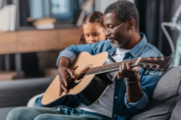 Мужчина играет на гитаре с дочерью дома — стоковое фото