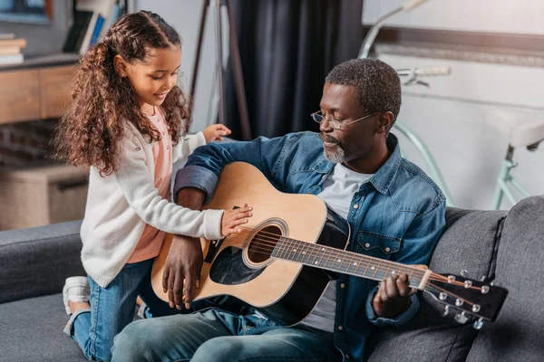 Hombre tocando la guitarra con su hija en casa - foto de stock