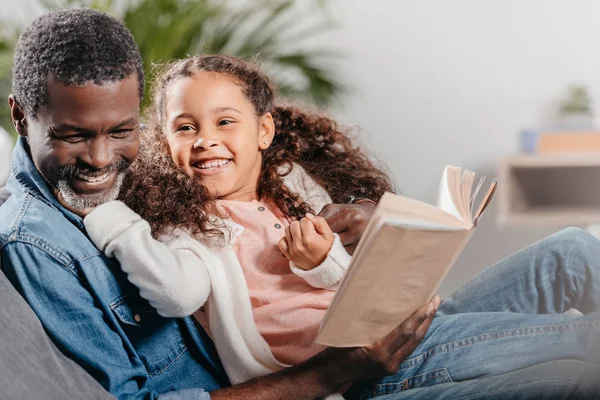 Мужчина читает книгу с дочерью дома — стоковое фото