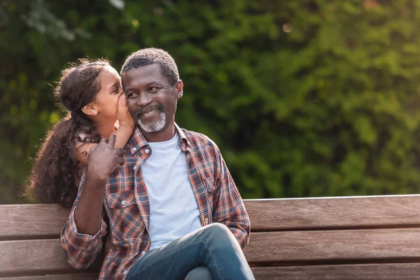 Kleines Mädchen flüstert ihrem Großvater zu — Stockfoto