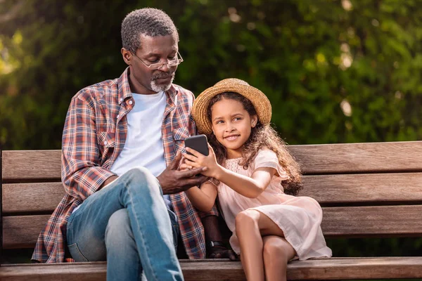 Girl and grandfather with smartphone in park — Stock Photo