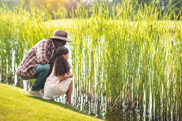 Nieta y abuelo sentado cerca del lago - foto de stock