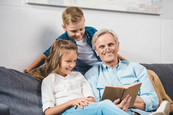 Famille utilisant laptopgrandpère et petits-enfants lecture livre — Photo de stock