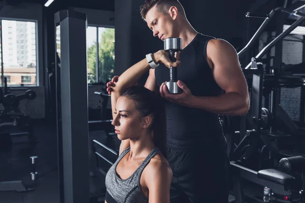 Entrenador ayudar a la mujer a hacer ejercicio con la mancuerna - foto de stock