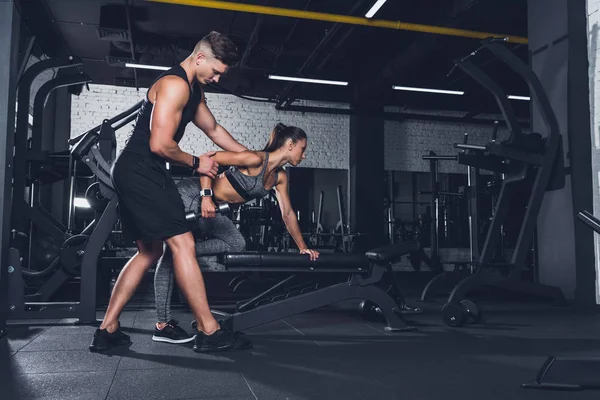 Entrenador ayudar a la mujer a hacer ejercicio con la mancuerna - foto de stock