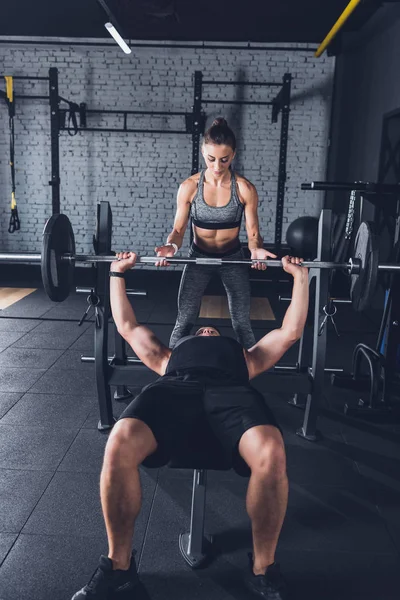 Woman helping man to lift barbell — Stock Photo