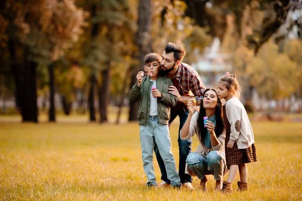 Padres con niños soplando burbujas - foto de stock