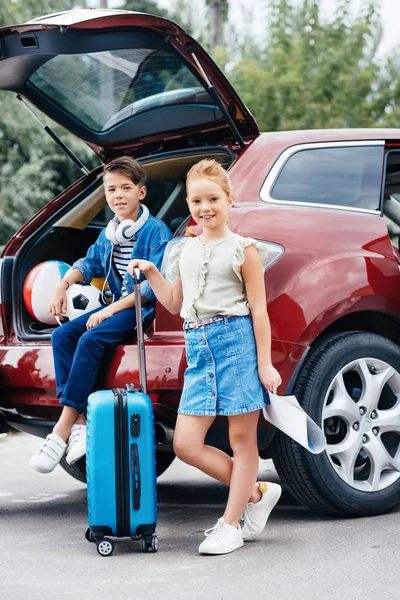 Niños con equipaje de pie junto al coche - foto de stock