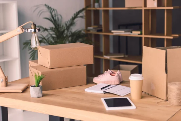 Freelance worker workplace with cardboard boxes, notebook and pair of shoes at home office — Stock Photo