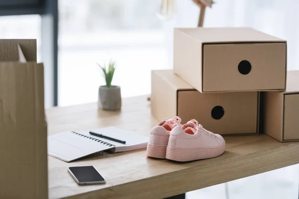 Freelance worker workplace with cardboard boxes, notebook and pair of shoes at home office — Stock Photo