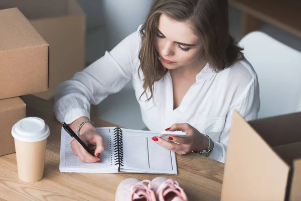 High angle view of businesswoman with smartphone in hand making notes — Stock Photo