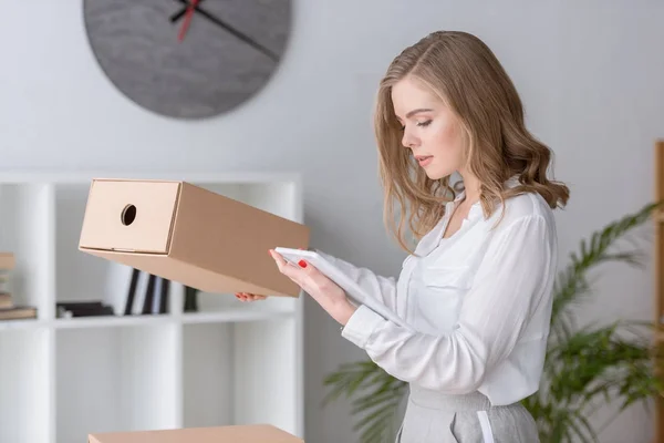 Portrait of young businesswoman with cardboard box and tablet in hands — Stock Photo