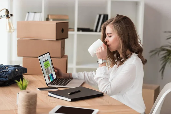 Vista laterale della donna d'affari che beve caffè mentre lavora sul computer portatile a tavola — Foto stock