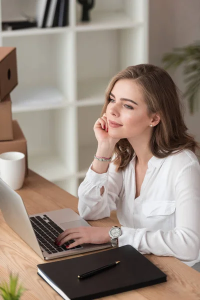 Vista lateral de la mujer de negocios pensativa mirando hacia otro lado mientras está sentado en la mesa con el ordenador portátil - foto de stock