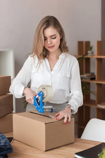 Portrait of young entrepreneur packing customers parcel with adhesive tape — Stock Photo