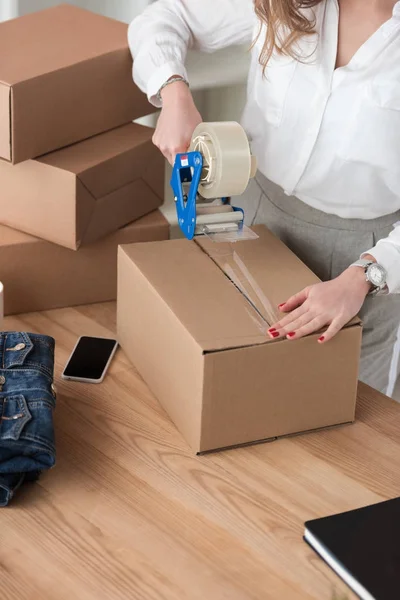 Partial view of entrepreneur packing customers parcel with adhesive tape — Stock Photo