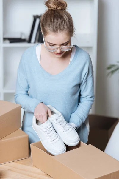 Entrepreneur putting shoes into cardboard box while packing customers purchase at home office — Stock Photo