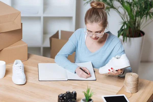 Portrait de jeune entrepreneur avec une paire de chaussures prenant des notes dans un carnet au bureau à domicile — Photo de stock