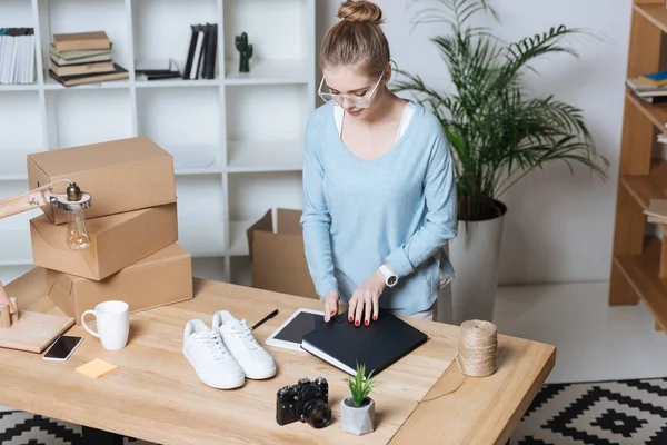 Vue grand angle du jeune entrepreneur debout sur le lieu de travail avec des boîtes en carton et un ordinateur portable au bureau à domicile — Photo de stock