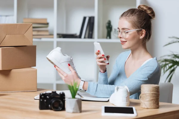 Propietario de la tienda en línea toma de fotos del producto en el teléfono inteligente en casa oficina - foto de stock