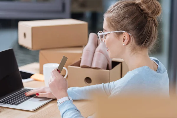 Selektiver Fokus der Frau mit Kreditkarte in der Hand, die auf den Laptop-Bildschirm am Tisch blickt — Stockfoto