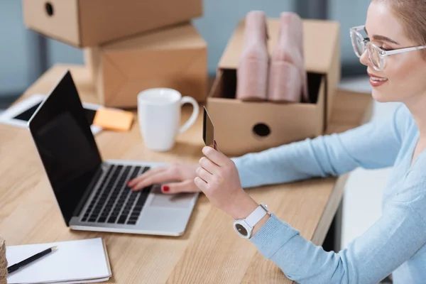 Selective focus of woman with credit card in hand looking at laptop screen at table — Stock Photo